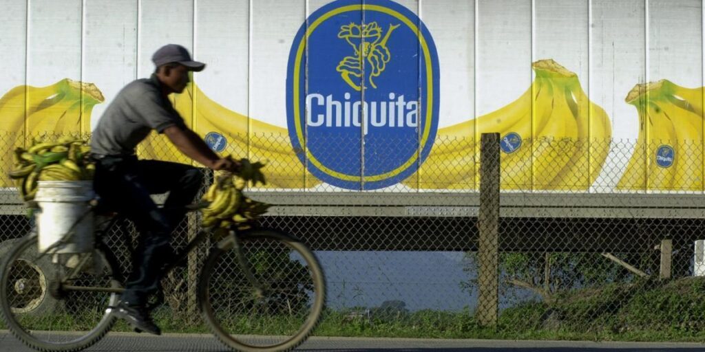 A farmer rides a bike loaded with plantains next to a truck with the logo of the US corporation Chiquita Banana. Photo: Esteban Felix/AP.