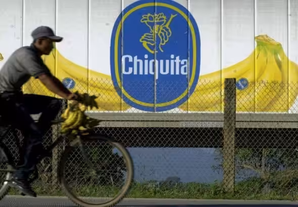 A farmer rides a bike loaded with plantains next to a truck with the logo of the US corporation Chiquita Banana. Photo: Esteban Felix/AP.