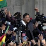 Bolivian President Luis Arce raises a clenched fist, surrounded by the public movements against the coup and by media, outside the government palace in La Paz, Bolivia, Wednesday, June 26, 2024. Photo: Juan Karita/AP.