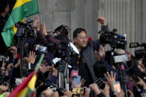 Bolivian President Luis Arce raises a clenched fist, surrounded by the public movements against the coup and by media, outside the government palace in La Paz, Bolivia, Wednesday, June 26, 2024. Photo: Juan Karita/AP.