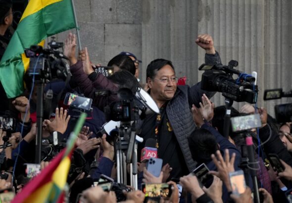 Bolivian President Luis Arce raises a clenched fist, surrounded by the public movements against the coup and by media, outside the government palace in La Paz, Bolivia, Wednesday, June 26, 2024. Photo: Juan Karita/AP.