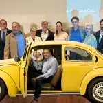 Venezuelan far-right presidential candidate Edmundo Gonzalez on the driver seat of a yellow Volkswagen Beetle, a campaign photo aimed at showing some connection to ordinary Venezuelans. In the background Maria Corina Machado and the creators of the "Land of Grace" neoliberal plan during its presentation in October 2023. Photo: X/@EdmundoGU and Vente Venezuela with image edition by Orinoco Tribune.