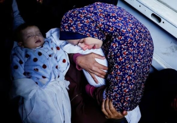 A Palestinian mother Rania Abu Anza holds one of her five-month old twins who were killed alongside her husband and 11 other relatives in an Israeli airstrike. Photo: @hamdahsalhut).