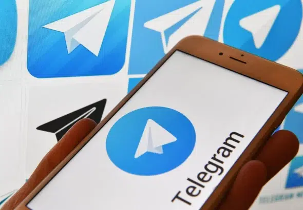Person holding a phone with the Telegram logo on the screen, in the background several logos of the Telegram social media platform. Photo: Natalia Seliverstova/Sputnik.