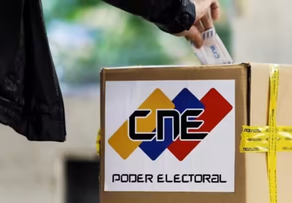 Person casting a paper ballot in a box with the logo of the Venezuelan National Electoral Council (CNE). Photo: File photo.