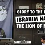 Poster depicting Palestinian Resistance martyr Ibrahim Babulsi holding a rifle, placed in a street next to a wooden door where a young girl passes by. With a caption reading :Glory to the martyr Ibrahim Nabulsi, the Lion of Nablus. Photo: Samidoun.