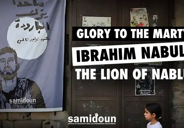Poster depicting Palestinian Resistance martyr Ibrahim Babulsi holding a rifle, placed in a street next to a wooden door where a young girl passes by. With a caption reading :Glory to the martyr Ibrahim Nabulsi, the Lion of Nablus. Photo: Samidoun.