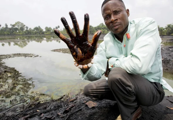 A Nigerian man holds up his hand to show oil sludge that has been polluting the Niger Delta region due to oil spills caused by the British petroleum giant Shell. Photo: The Guardian.