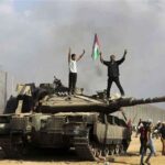 Palestinians stand atop a captured Israeli tank and wave a Palestinian flag on October 7, 2023. Photo: Yousef Masoud/AP.