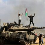 Gaza residents celebrate by a destroyed Israeli tank, east of Khan Younis, October 7, 2023. Photo: AP.