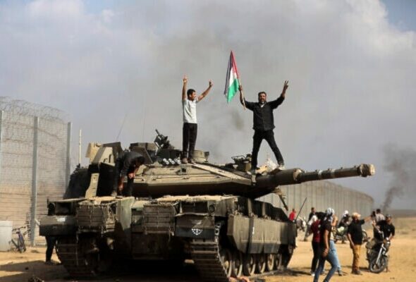 Gaza residents celebrate by a destroyed Israeli tank, east of Khan Younis, October 7, 2023. Photo: AP.