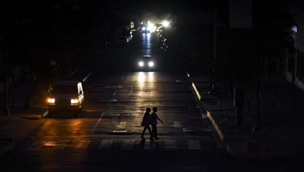Two persons cross a street while cars pass by them, during one of the regular blackouts in Quito, Ecuador. Photo: El Nacional.