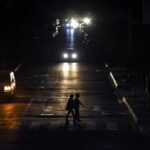 Two persons cross a street while cars pass by them, during one of the regular blackouts in Quito, Ecuador. Photo: El Nacional.