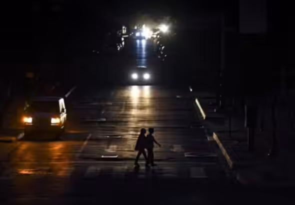 Two persons cross a street while cars pass by them, during one of the regular blackouts in Quito, Ecuador. Photo: El Nacional.