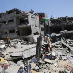 People raise a Palestinian flag next to their house destroyed by an Israeli airstrike in the Bureij refugee camp in the southern Gaza Strip. Photo: Mohammed Sable/EFE.