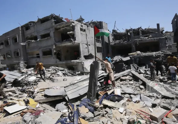 People raise a Palestinian flag next to their house destroyed by an Israeli airstrike in the Bureij refugee camp in the southern Gaza Strip. Photo: Mohammed Sable/EFE.