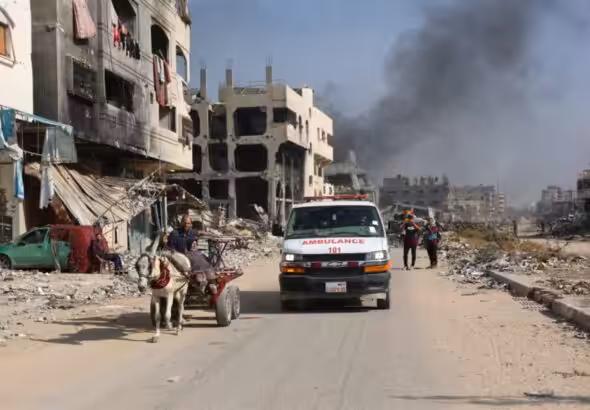 An ambulance drives through a devastated neighborhood in Gaza, passing by civilians using a horse-drawn cart amidst widespread destruction caused by ongoing airstrikes. Photo: AFP.