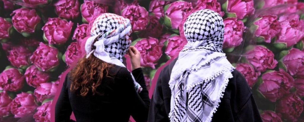 Two people wearing keffiyehs stand facing a wall covered in flowers. Photo: Institute for Palestine Studies.