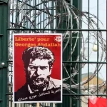 A poster reading 'Freedom for Georges Abdallah' is placed near razor wire on the gate outside the prison in southern France on October 25, 2014. Photo: AFP.