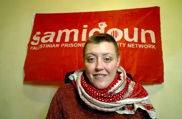 Charlotte Kates in front of a red Samidoun banner. Photo: teleSUR.