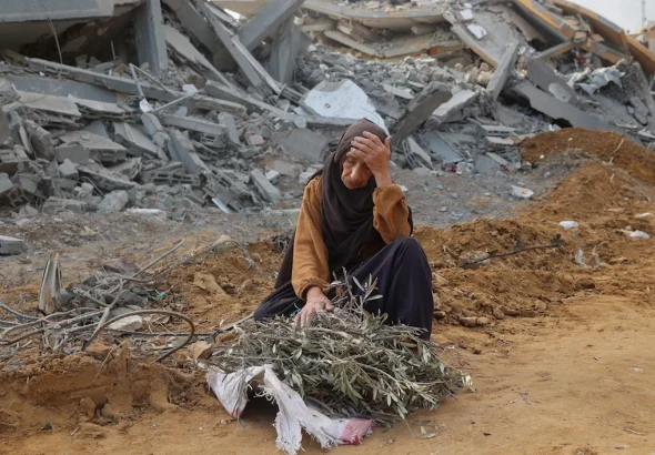 A Palestinian woman sits amid rubble, holding olive branches, reflecting the wider loss and devastation in Gaza. Photo: AFP.