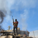 A Palestinian resistance fighter stands atop a burning "Israeli" tank on October 7, 2023. Photo: Hani Alshaer/AA/Getty Images.