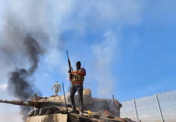 A Palestinian resistance fighter stands atop a burning "Israeli" tank on October 7, 2023. Photo: Hani Alshaer/AA/Getty Images.