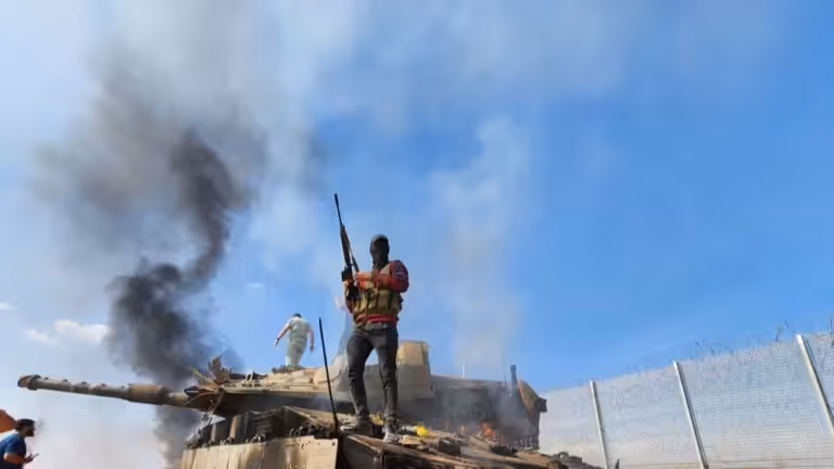 A Palestinian resistance fighter stands atop a burning "Israeli" tank on October 7, 2023. Photo: Hani Alshaer/AA/Getty Images.
