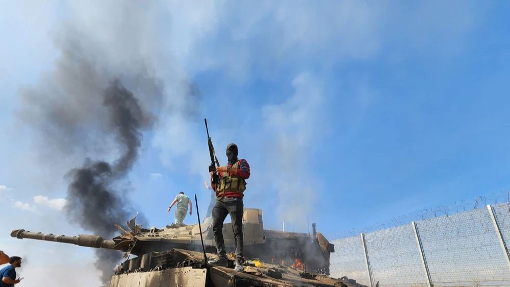 A Palestinian resistance fighter stands atop a burning "Israeli" tank on October 7, 2023. Photo: Hani Alshaer/AA/Getty Images.