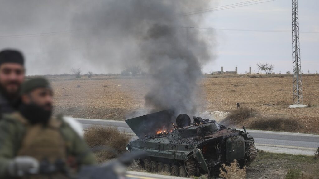 Extremist militants ride past an overturned Syrian army tank on fire. Photo: Ghaith Alsayed/AP.