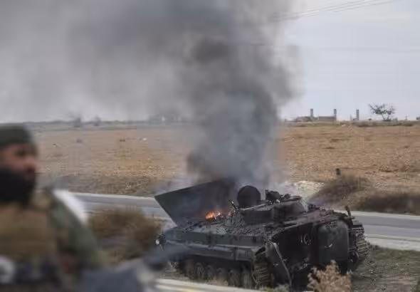 Extremist militants ride past an overturned Syrian army tank on fire. Photo: Ghaith Alsayed/AP.