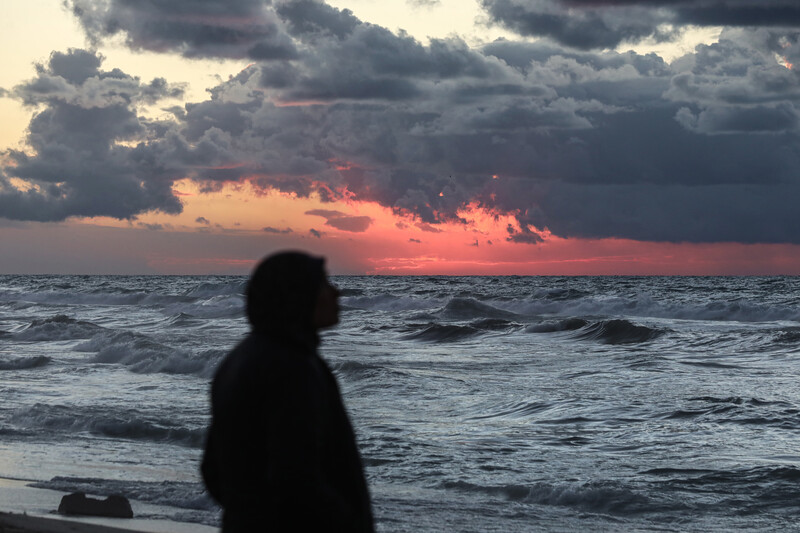 Palestinians walk on the beach during sunset on the last day of 2024 in Deir al-Balah in the central Gaza Strip, on 31 December 2024. Photo: Omar Ashtawy/APA images.