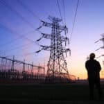 Power lines and a worker at sunset. Photo: Zhengzaishuru/Getty Images.