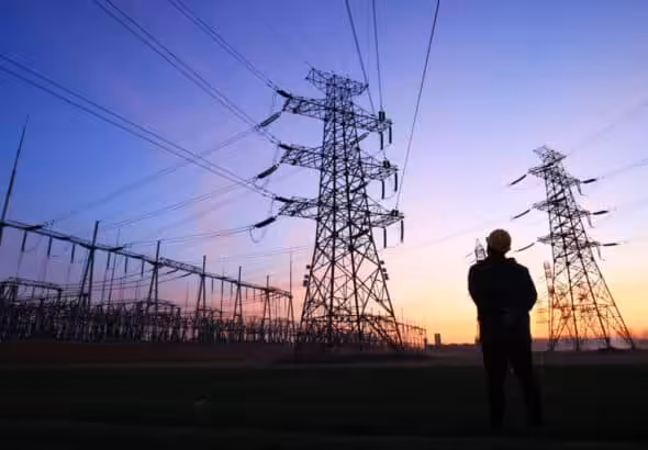 Power lines and a worker at sunset. Photo: Zhengzaishuru/Getty Images.