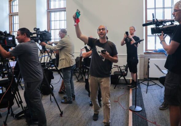 Yves Engler waves a Palestinian flag at Montreal Mayor Valérie Plante's press conference at Montreal city hall, July 5, 2024, protesting the police repression against a pro-Palestine encampment in Victoria Square. Photo: John Kenney/The Montreal Gazette.