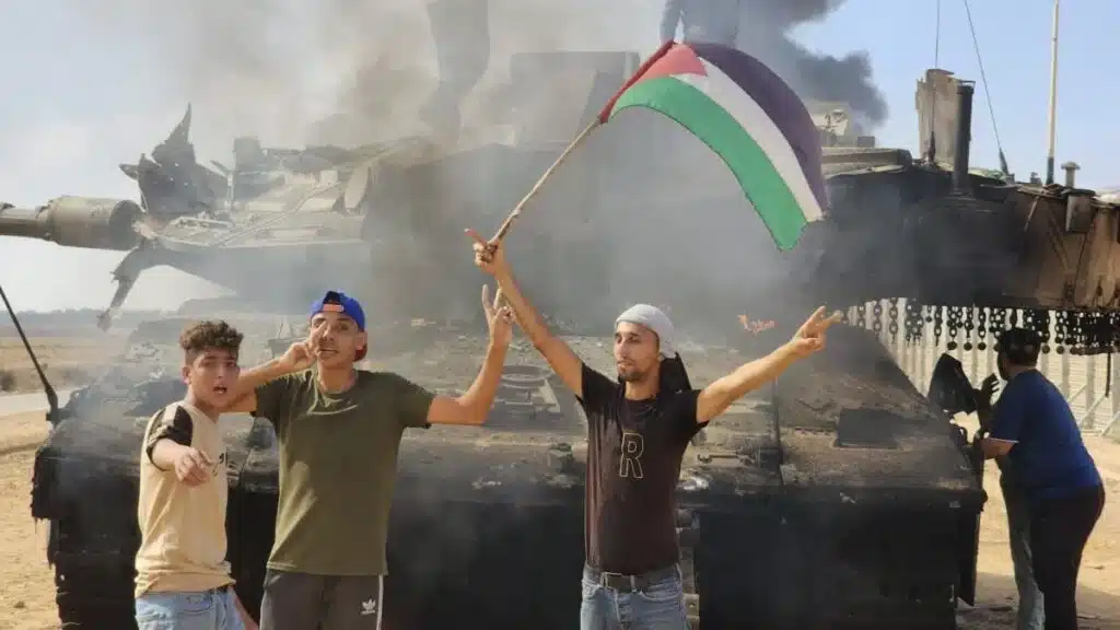 Personas ondeando una bandera palestina frente a un tanque israelí destruido. Foto de archivo.