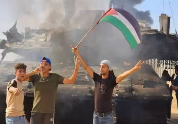 People waving a Palestinian flag in front of a destroyed Israeli tank. File photo.