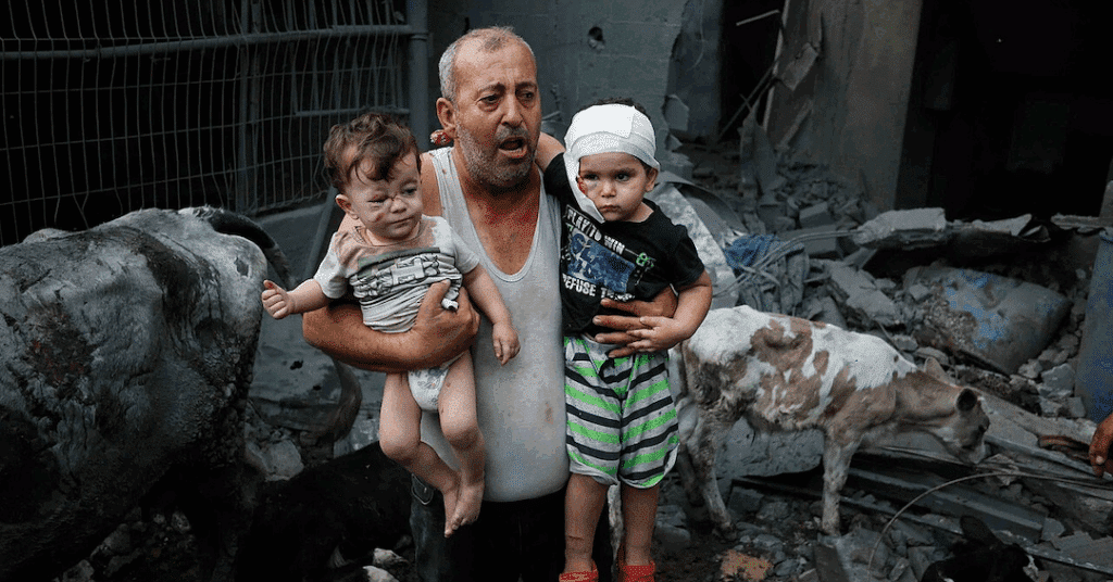 A Palestinian refugee carries his injured grandchildren from the Israeli bombing of Nuseirat Camp, Gaza Strip. Photo: Ashraf Amra/2023 UNRWA.