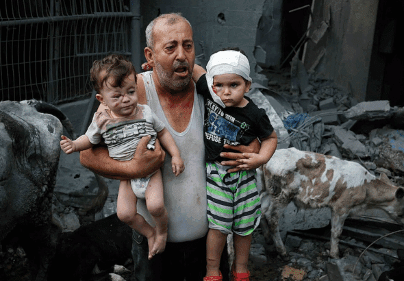 A Palestinian refugee carries his injured grandchildren from the Israeli bombing of Nuseirat Camp, Gaza Strip. Photo: Ashraf Amra/2023 UNRWA.
