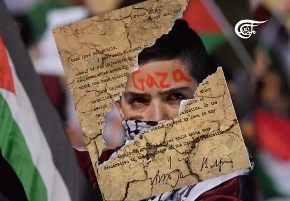 Photo composition showing a torn version of the Balfour Declaration superimposed over a photo of a youth holding a Palestinian flag and with the word "Gaza" written on his forehead. Photo: Al Mayadeen.