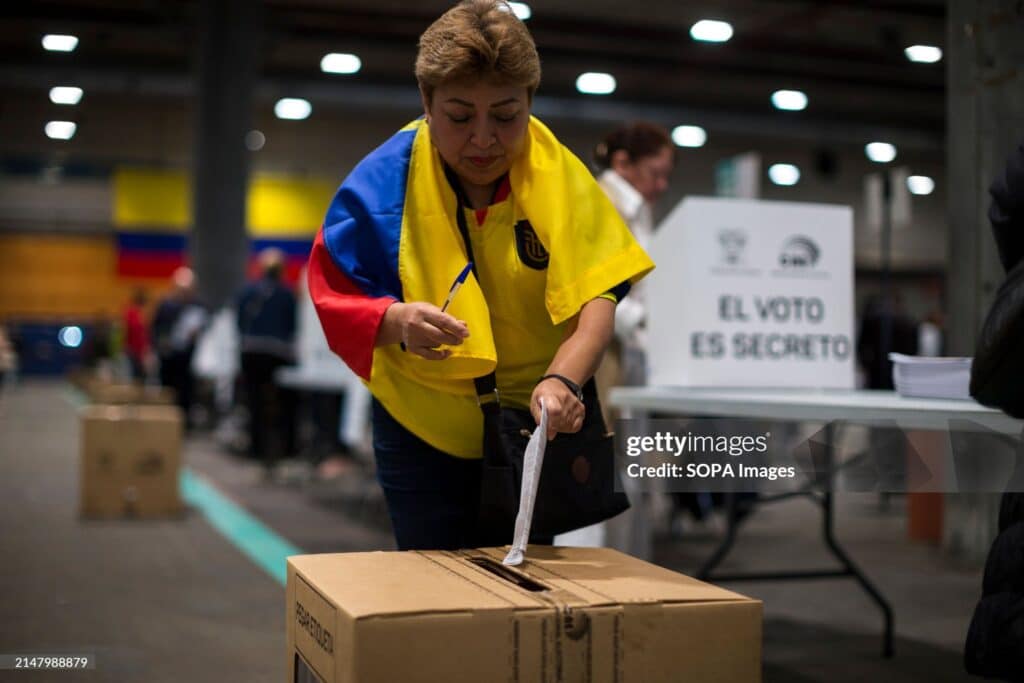 MADRID, SPAIN - 2024/04/21: A woman with an Ecuadorian flag around her neck casts her vote into the ballot box at one of the voting tables at the IFEMA fairgrounds in Madrid, during the referendum day in Ecuador. The Ecuadorian community registered in Madrid exceeds 60,000 and can exercise their right to vote for people from abroad, in the referendum proposed by President Daniel Noboa in the face of growing violence in Ecuador. Photo: Luis Soto/Getty Images.