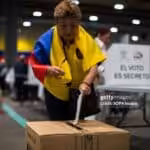 MADRID, SPAIN - 2024/04/21: A woman with an Ecuadorian flag around her neck casts her vote into the ballot box at one of the voting tables at the IFEMA fairgrounds in Madrid, during the referendum day in Ecuador. The Ecuadorian community registered in Madrid exceeds 60,000 and can exercise their right to vote for people from abroad, in the referendum proposed by President Daniel Noboa in the face of growing violence in Ecuador. Photo: Luis Soto/Getty Images.