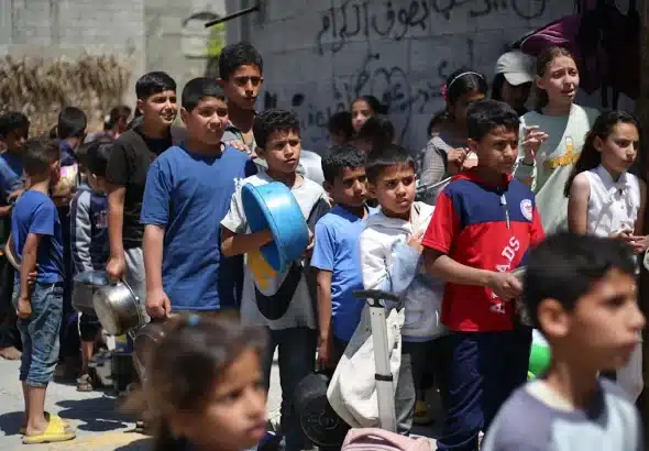 Dozens of children formed a long line outdoors, carrying containers such as pots, buckets, and makeshift containers to receive food. Photo: AFP.