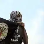 Youth in a keffiyeh holding a resistance flag. Photo: Haitham Moussawy.