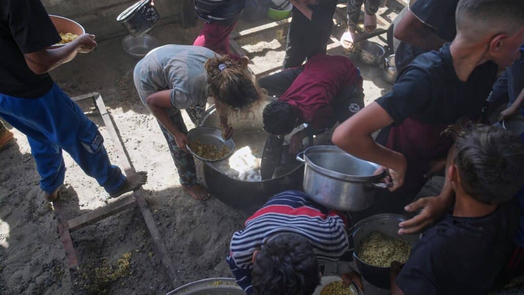 Palestinian children scrape a pot for leftover food after all meals were distributed at a community kitchen in Khan Younis, southern Gaza Strip, on Friday, May 9, 2025. Photo: AP/Abdel Kareem Hana.