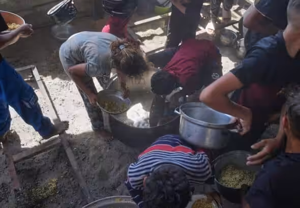 Palestinian children scrape a pot for leftover food after all meals were distributed at a community kitchen in Khan Younis, southern Gaza Strip, on Friday, May 9, 2025. Photo: AP/Abdel Kareem Hana.