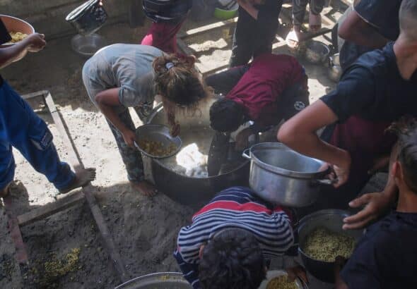 Palestinian children scrape a pot for leftover food after all meals were distributed at a community kitchen in Khan Younis, southern Gaza Strip, on Friday, May 9, 2025. Photo: AP/Abdel Kareem Hana.