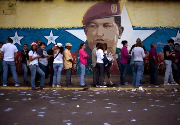 Line of voters in front of a wall bearing a mural of Hugo Chávez. Photo: AP/Ariana Cubillos/file photo.