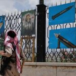 A Yemeni gunman walks past paintings of rockets and scenes of solidarity with Gaza, displayed on a fence in Sana'a, Yemen, May 5, 2025. Photo: AP.