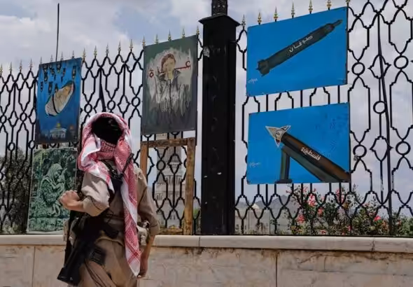 A Yemeni gunman walks past paintings of rockets and scenes of solidarity with Gaza, displayed on a fence in Sana'a, Yemen, May 5, 2025. Photo: AP.
